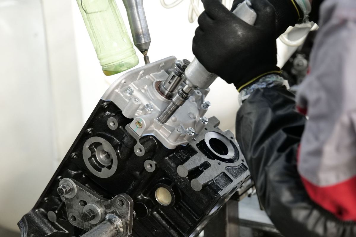 Mãos com luvas montando componentes de motor com ferramenta pneumática na bancada